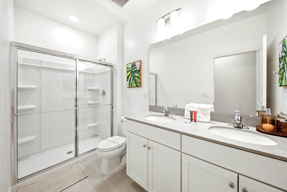 This bright bathroom boasts sleek white cabinetry and a spacious glass-enclosed shower, creating a fresh atmosphere. Natural light enhances the modern fixtures and vibrant artwork, adding a unique touch for your comfort.
