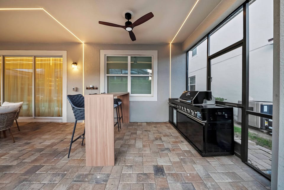 Discover this charming outdoor space with a sleek black grill and stylish bar seating, ideal for casual gatherings. Warm lighting accentuates the textured tile flooring, creating a cozy atmosphere perfect for relaxation.
