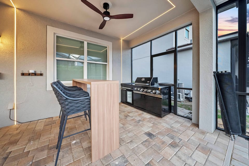 This outdoor space offers a stylish bar with sleek wicker stools, perfect for enjoying a drink while the grill sizzles nearby. The warm lighting and tile flooring create a welcoming atmosphere, ideal for relaxed evenings.