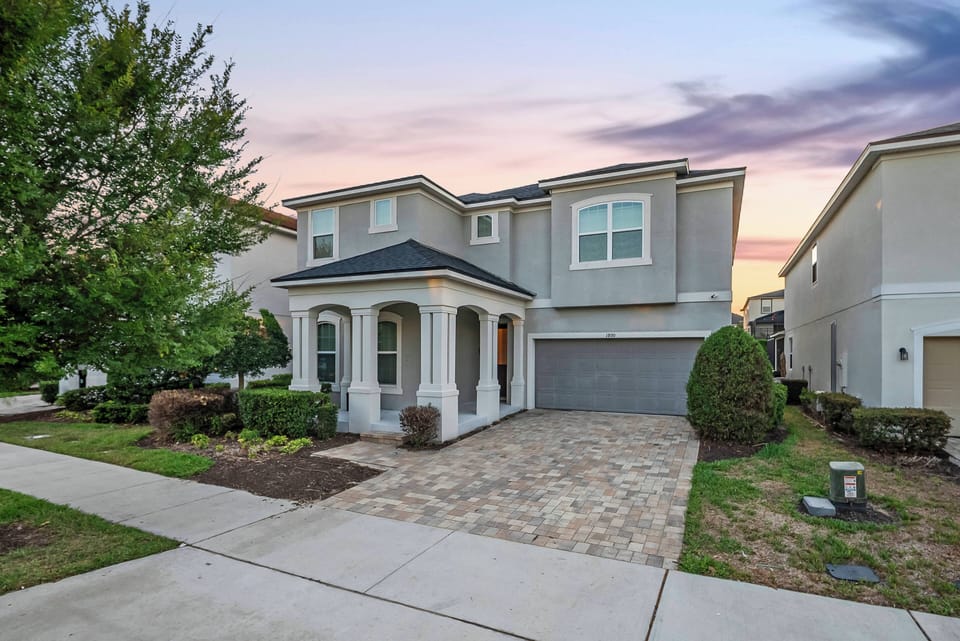 Step into a charming exterior featuring a stone-paved driveway and welcoming porch, framed by well-kept greenery. The soft hues of the evening sky create a picturesque backdrop, setting the stage for your stay.