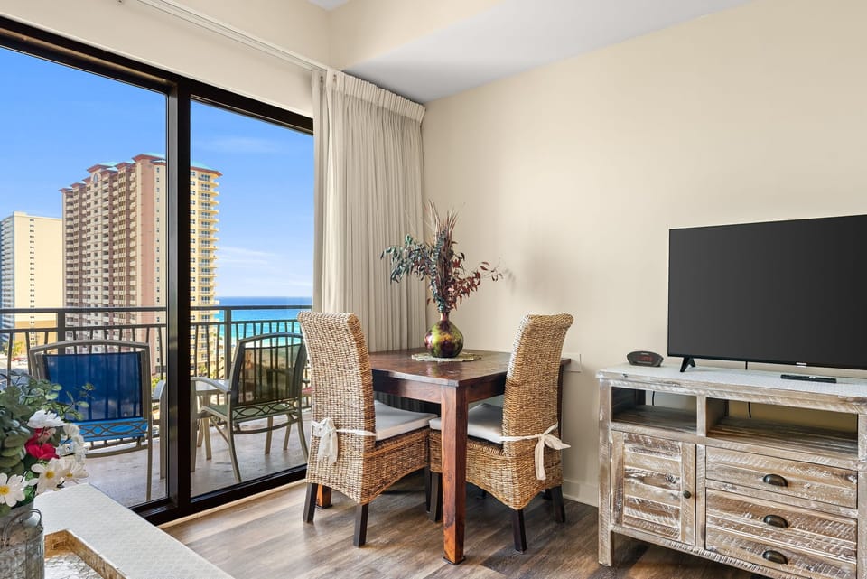 Your cozy dining nook features wicker chairs and a warm wood table, with ocean glimpses through sliding doors to your private balcony.