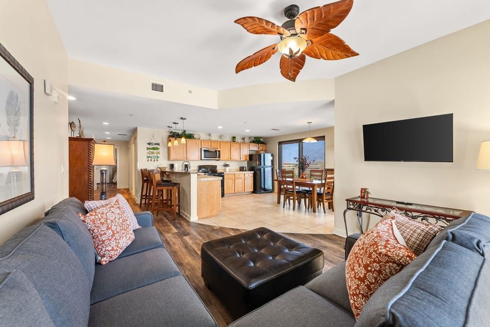 Relax in your spacious open-concept living area with tropical ceiling fan, plush sectional seating, and seamless flow to your fully equipped kitchen.
