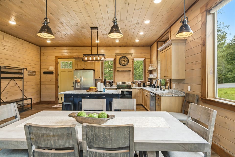 Gather around your spacious dining table or chat at the kitchen island while preparing meals together. Natural light pours through large windows, warming the wood-paneled walls and creating a welcoming space for your group.