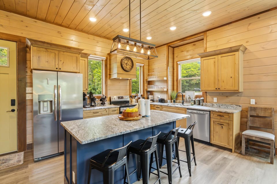 Step into your cabin-style kitchen with warm wood walls and modern amenities. Gather around the spacious island with friends, cook up a feast with stainless appliances, and enjoy natural light streaming through the windows.