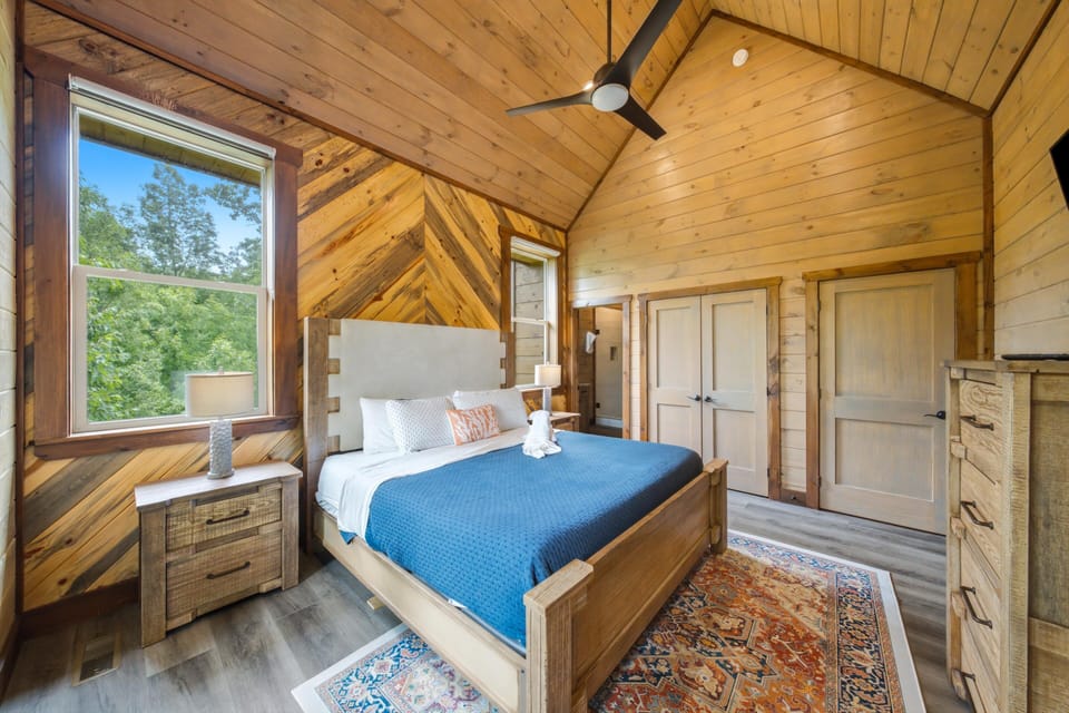 Sink into the blue quilt of your rustic retreat with soaring timber ceilings and a leafy view that brings the outdoors right to your bedside. Unwind under soft light and feel the warmth of natural wood all around.