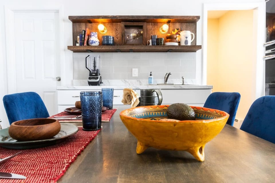 Fully equipped kitchen featuring a refrigerator, sink, stove, microwave, and Instant Pot, along with essential cooking supplies. A farmhouse table seats four, perfect for shared meals. Handcrafted rustic floating shelves, vintage touches, and dimmable lig