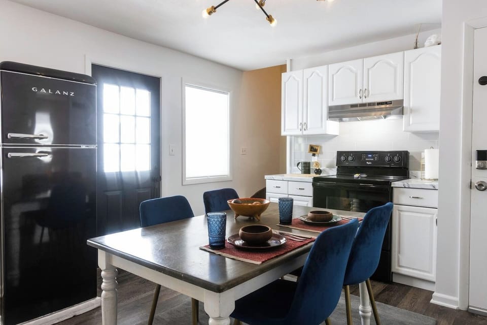 Fully equipped kitchen featuring a refrigerator, sink, stove, microwave, and Instant Pot, along with essential cooking supplies. A farmhouse table seats four, perfect for shared meals. Handcrafted rustic floating shelves, vintage touches, and dimmable lig