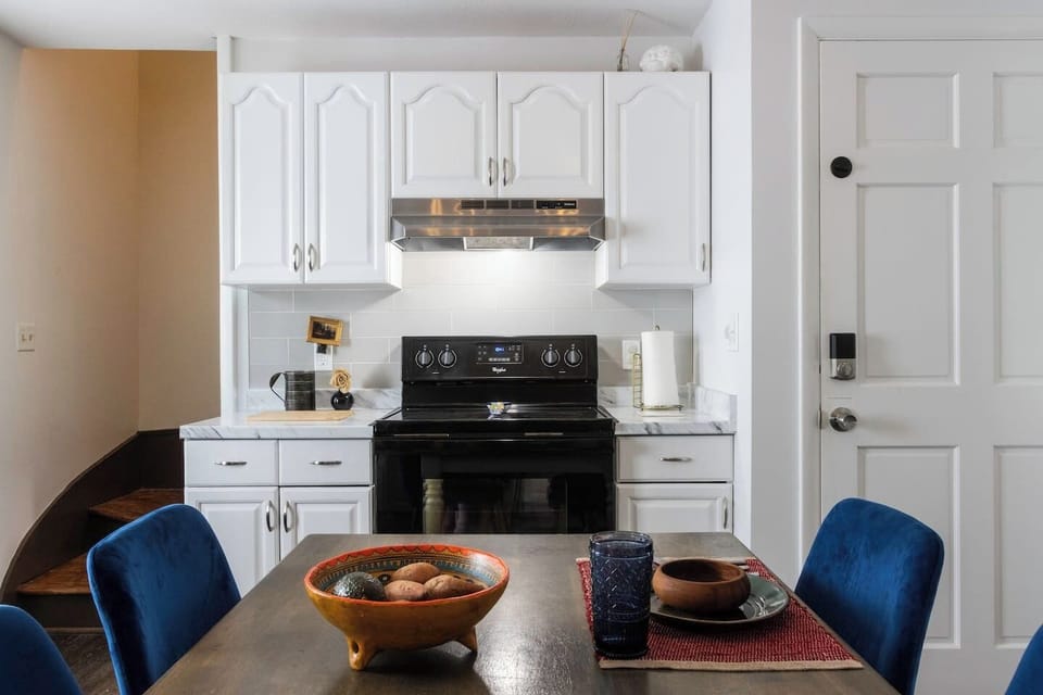 Fully equipped kitchen featuring a refrigerator, sink, stove, microwave, and Instant Pot, along with essential cooking supplies. A farmhouse table seats four, perfect for shared meals. Handcrafted rustic floating shelves, vintage touches, and dimmable lig