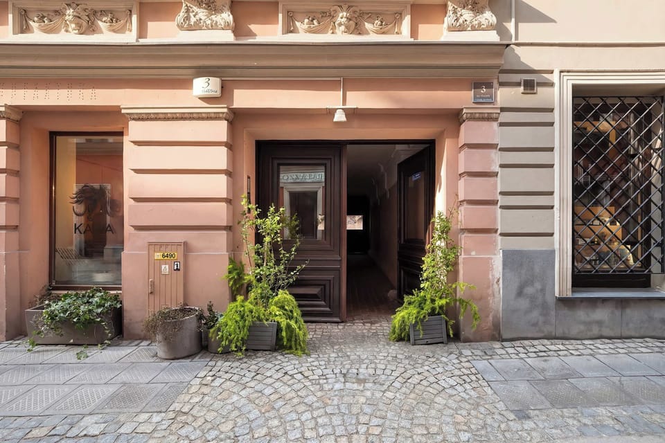 The entrance to a building with a soft pink exterior and potted plants by the doorway. The design feels welcoming and well-maintained.