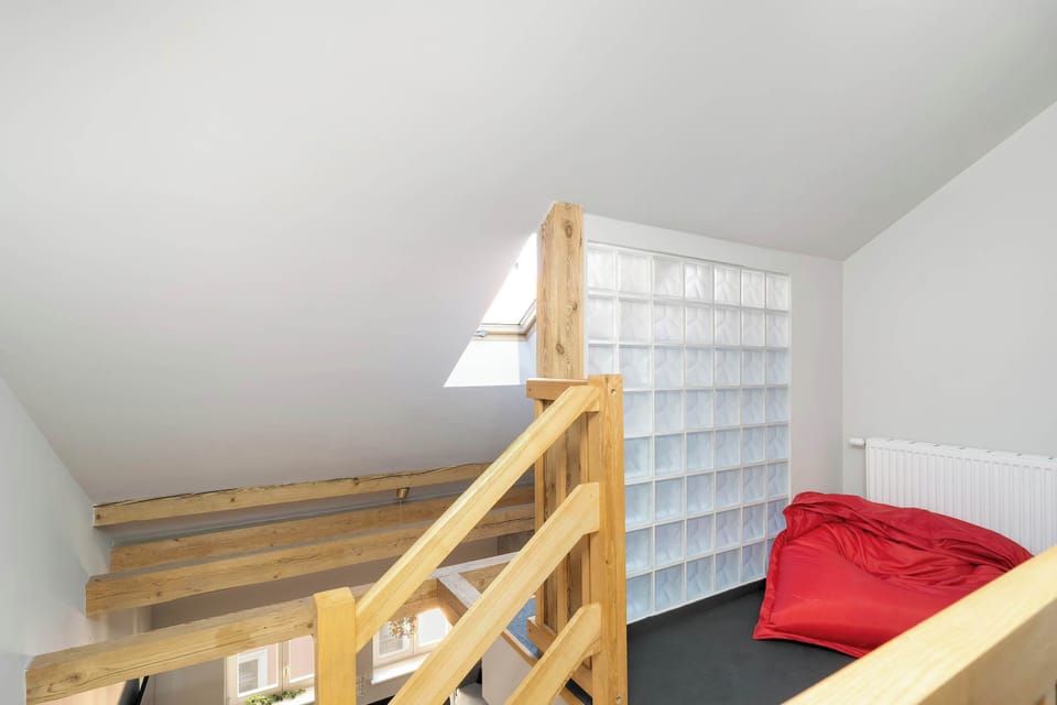 A staircase leading to the upper floor, partially carpeted, with a red cushion on the steps. Wooden handrails and natural light add warmth.