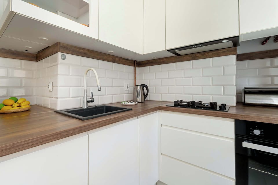 A modern, white L-shaped kitchen offers a built-in electric stovetop and oven, wood-grain countertops, and a subway tile backsplash.
