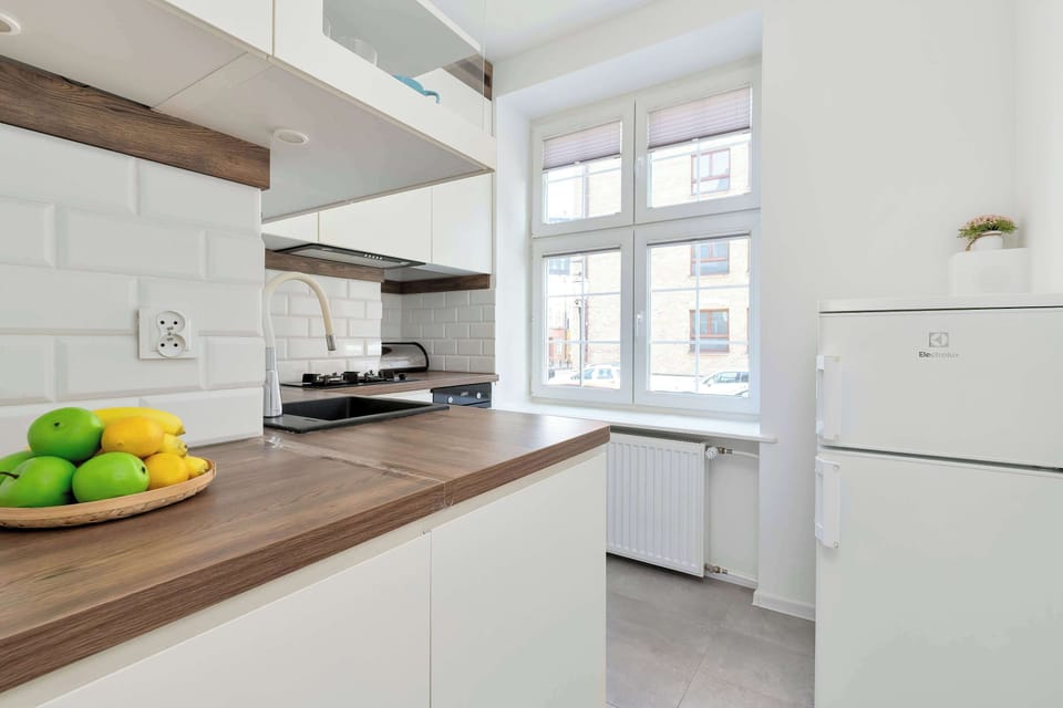 The sleek white kitchen features extensive counter space, a refrigerator, and a window overlooking the street.