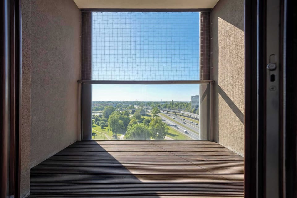 An enclosed balcony  with wooden flooring and safety netting. Large openings allow fresh air and views outside.