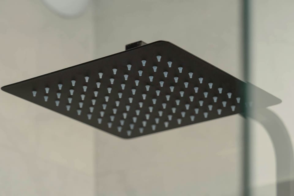 A focused shot shows a contemporary square rain shower head in a matte black finish. This high-end fixture promises a luxurious and relaxing shower experience for guests.