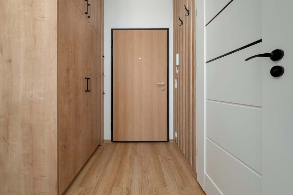The entryway features built-in wooden closets that offer ample storage for coats and shoes. A simple wooden door serves as the main entrance, maintaining the apartment's cohesive design.