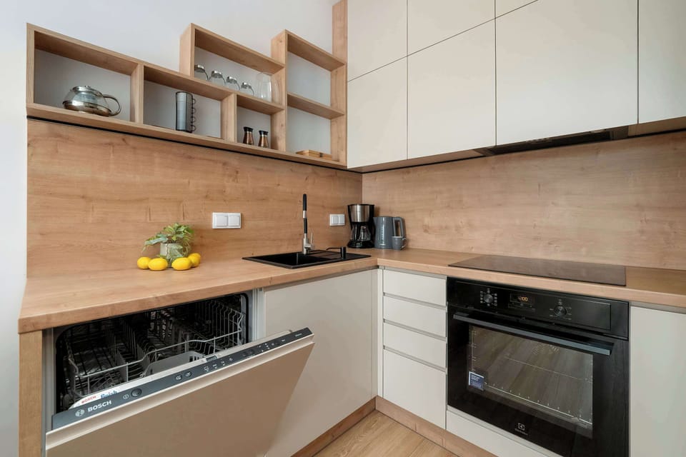 This perspective of the kitchenette reveals an integrated dishwasher and a modern black sink. The combination of light grey fronts and wood finishes creates a sophisticated, high-end look.