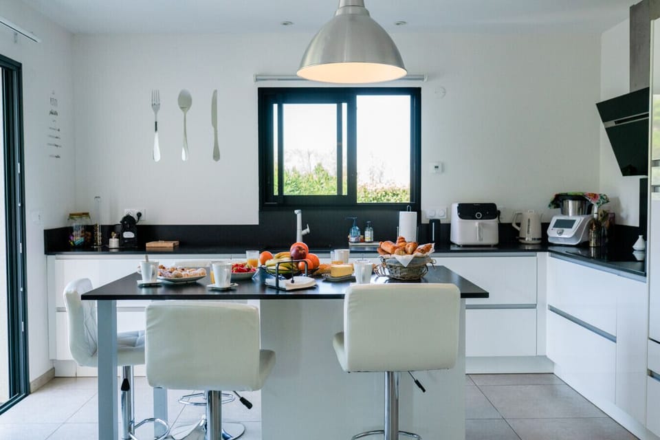 Cuisine ouverte avec coin repas – table, chaises blanches, plan de travail généreux et lumière naturelle par la fenêtre