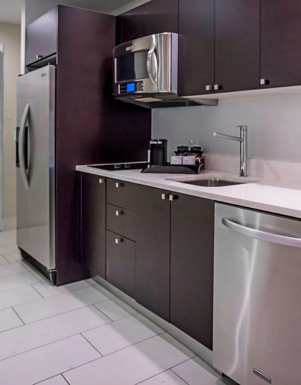Modern kitchenette with full-size refrigerator, microwave, sink, and contemporary cabinetry for convenient in-room dining.