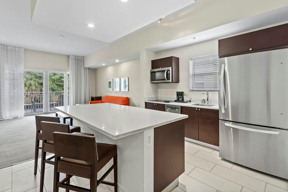 Stylish kitchen view highlighting the island workspace, full-size refrigerator, and clean, modern finishes.