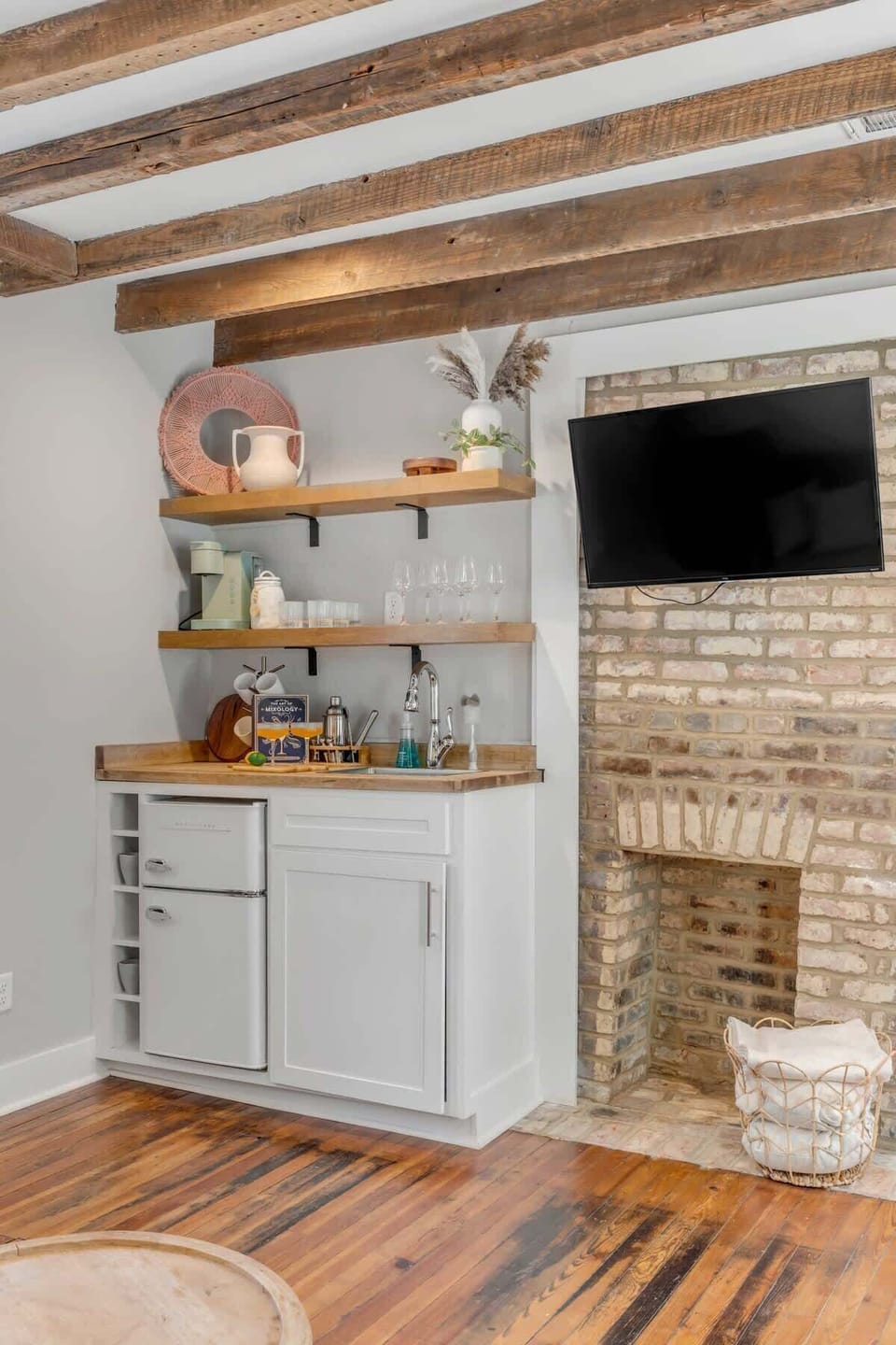 A welcoming living space with comfortable seating, a TV, and a stylish kitchenette featuring a coffee maker and wine glasses.