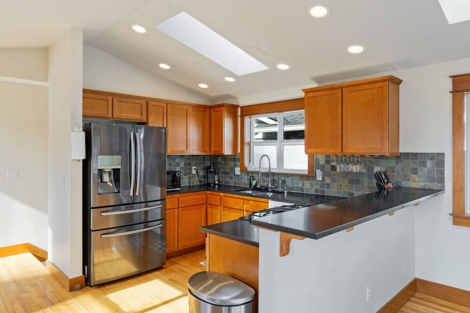 Well-equipped kitchen w/ stainless steel appliances, dark countertops & warm wood cabinetry.