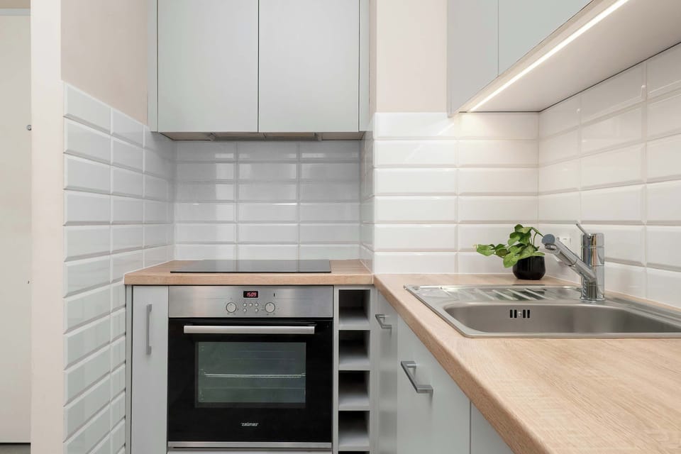 A minimalist-style kitchen area features modern gray and white cabinets, a light-colored wooden countertop with white subway tiles, and stainless steel appliances.