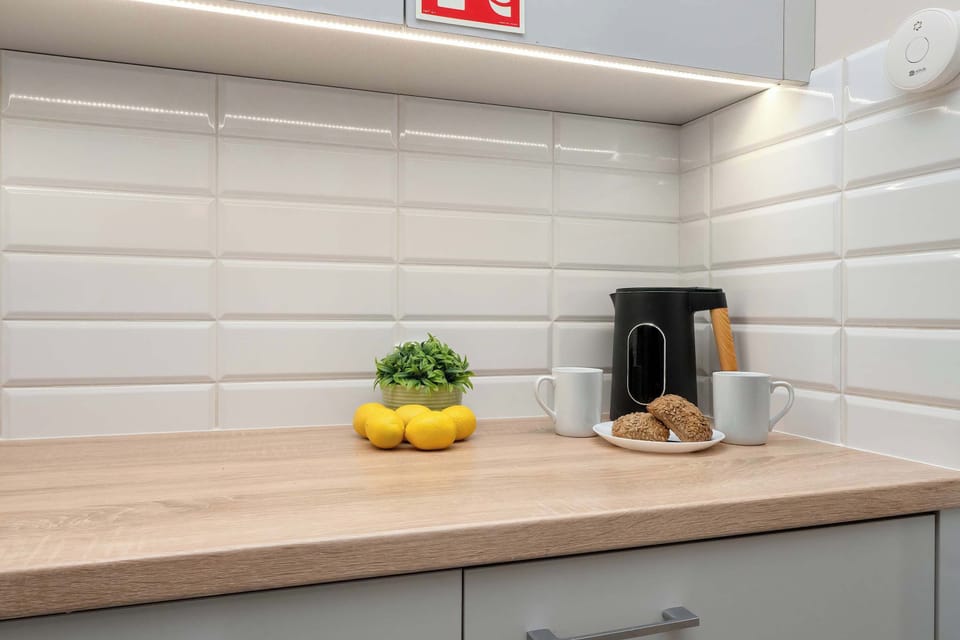 A minimalist-style kitchen area features a light-colored wooden countertop with white subway tiles, a metal pot with yellow lemons, and small glass jars.