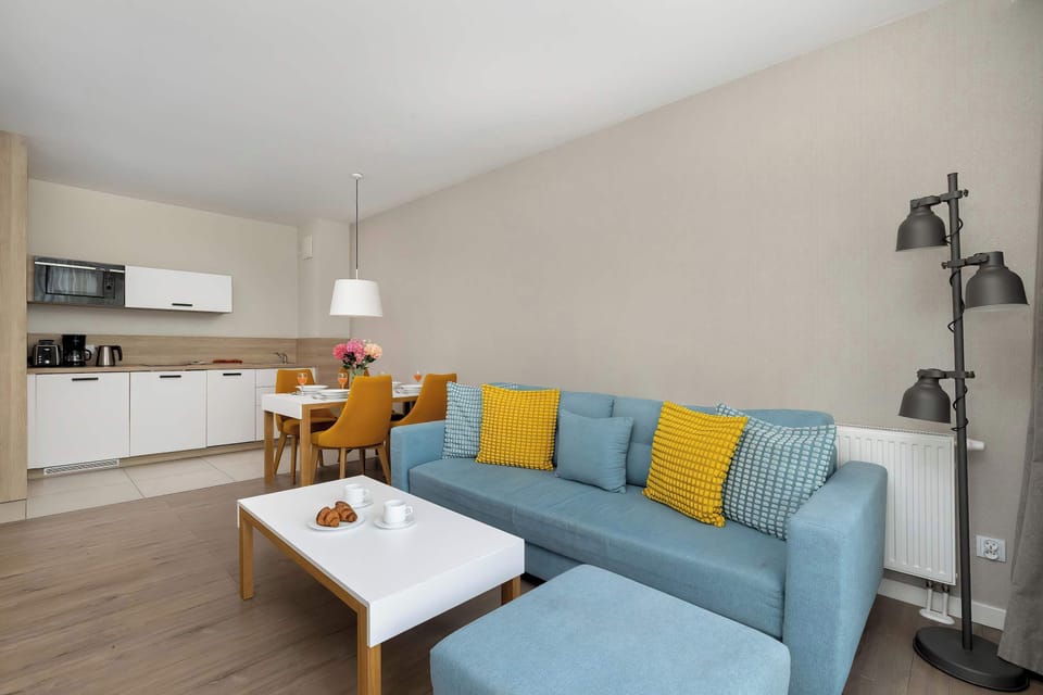 This open-plan view shows the seamless transition between the white kitchenette and the blue seating area. A tall, black floor lamp stands in the corner, adding a modern industrial touch to the space.