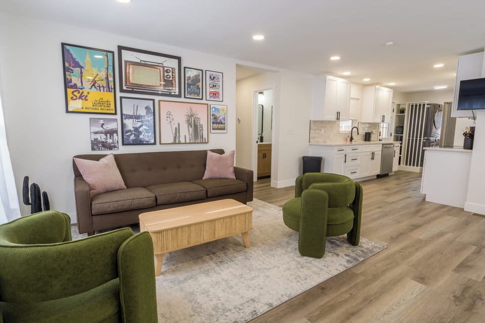 Sink into your stylish living room with vintage ski art and plush green chairs, flowing seamlessly into your modern kitchen.