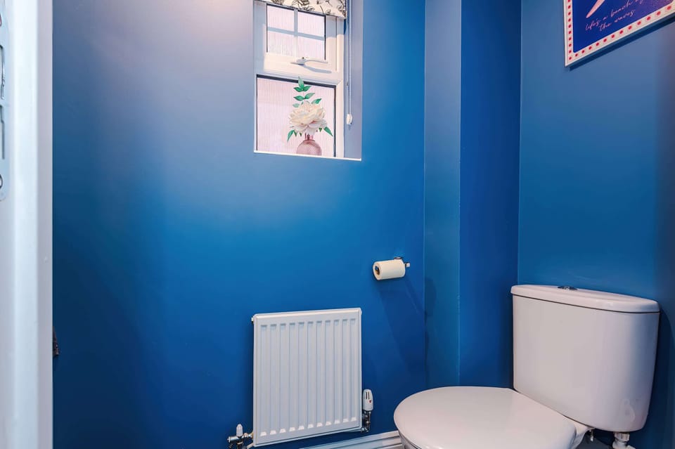 Enjoy a compact bathroom with blue tones, a bright window, and practical essentials. A radiator and tasteful décor make this space both efficient and inviting