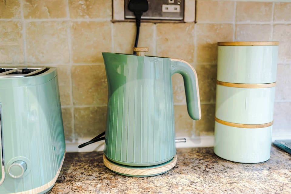 Stylish kitchen with muted green cabinets, granite countertops, and stainless steel appliances. Includes a large gas stove, washing machine, and window with leafy curtains—bright, functional space ideal for cooking and laundry convenience during your