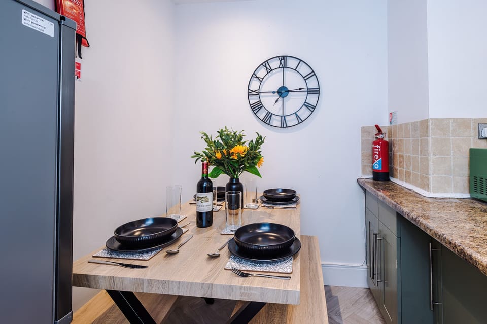 Stylish kitchen with muted green cabinets, granite countertops, and stainless steel appliances. Includes a large gas stove, washing machine, and window with leafy curtains—bright, functional space ideal for cooking and laundry convenience during your