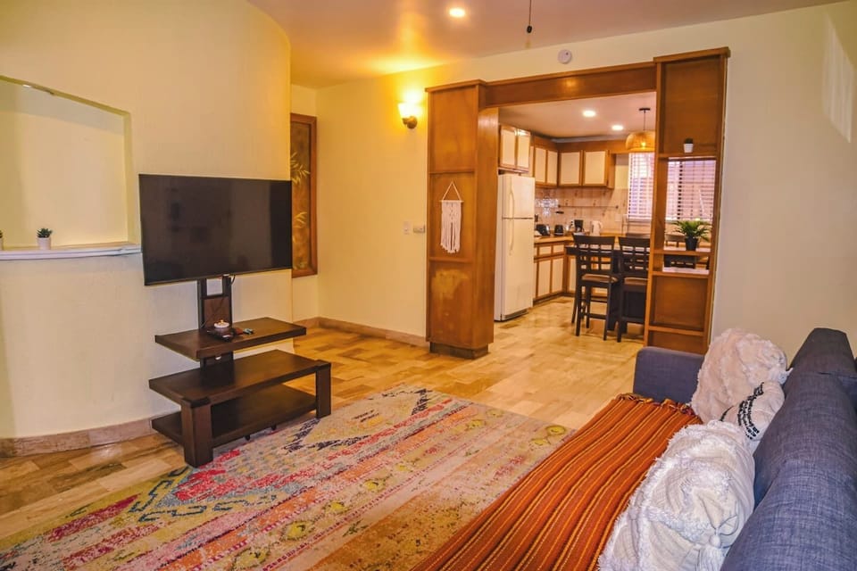 Bright, spacious living room with modern style and bohemian touches, perfect for couples or solo travelers. Cozy gray sofa, colorful rug, warm lighting, and an open layout with the kitchen create a welcoming space to relax or work.