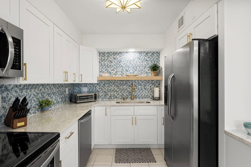 Bright and modern kitchen featuring quartz counters, stainless steel appliances, and elegant gold accents. Fully stocked with cookware and essentials, it’s perfect for preparing meals during your Panama City Beach getaway at The Breakers View condo.