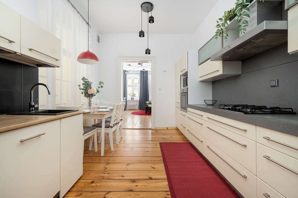 The long, modern kitchen displays sleek cream cabinetry paired with dark countertops and a red runner rug on the wooden floor. Built-in appliances and a gas stovetop are integrated into the functional workspace.