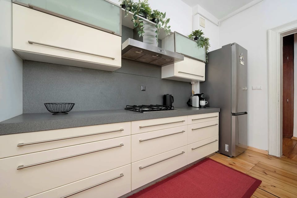 The kitchen cabinets are shown from a low angle, highlighting the clean lines of the cream drawers and the grey backsplash. A red rug adds a stripe of color to the traditional wooden floor.