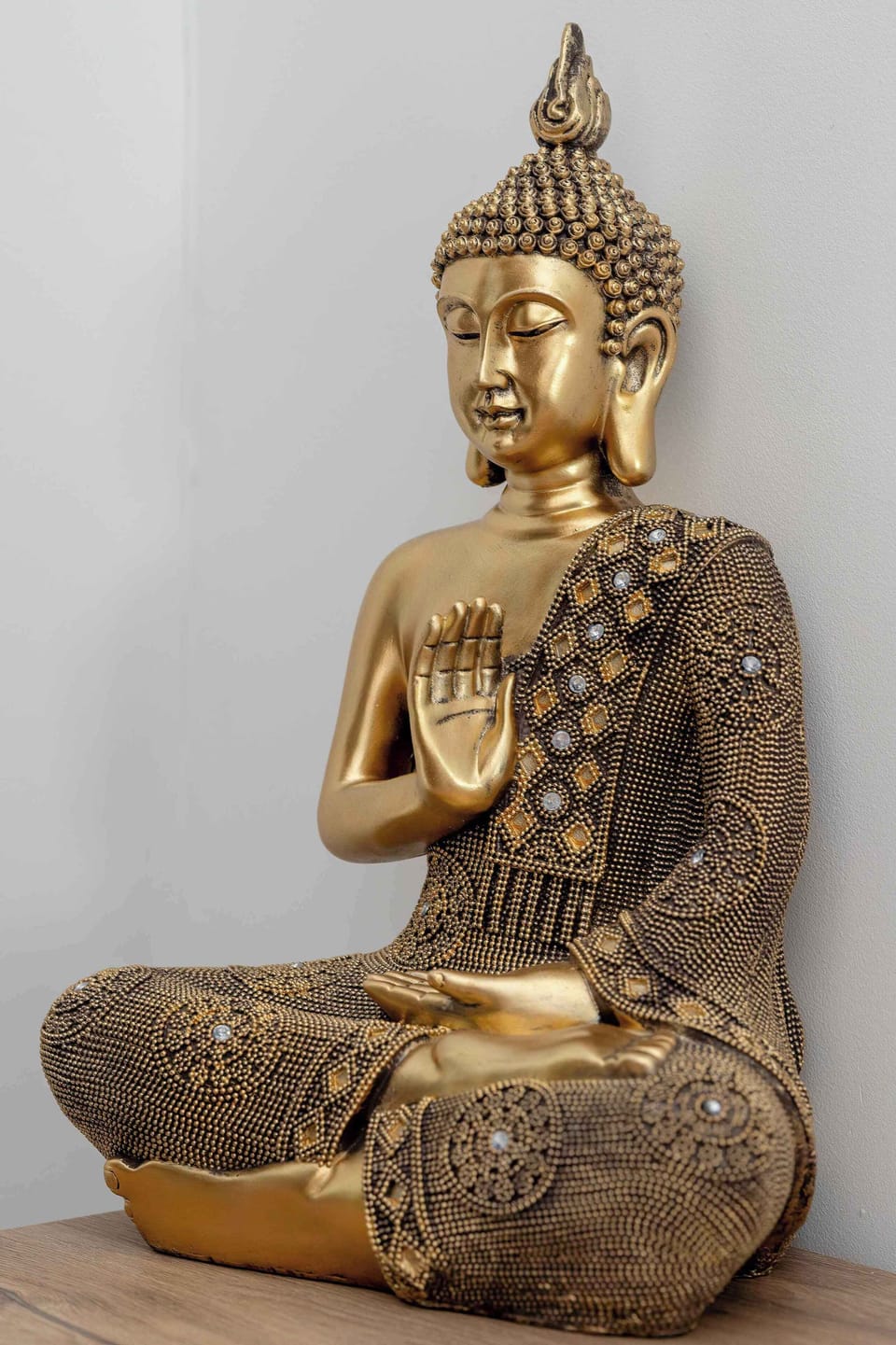 A golden Buddha statue sitting in a meditative pose against a light background. The sculpture looks polished and decorative. It adds a calm, spiritual element to the interior decor.