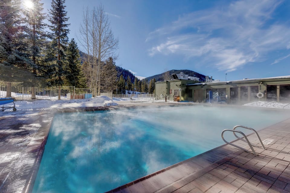 Heated outdoor pool surrounded by snow-covered mountains creates perfect winter relaxation with steam rising from warm waters.