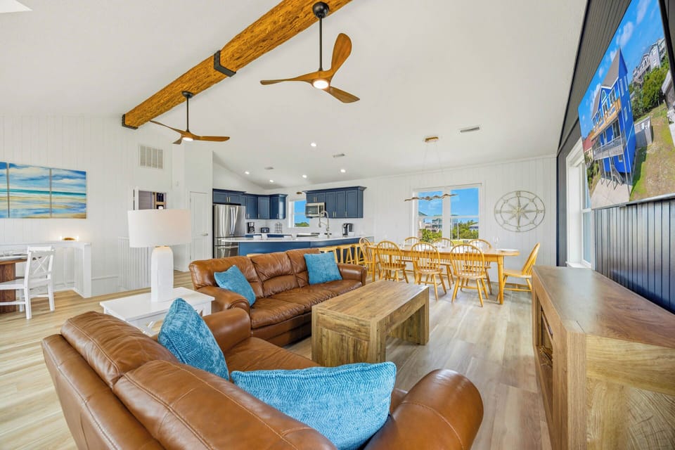 Settle into this bright, open living space where rustic wood beams meet coastal charm—your perfect retreat for gathering with loved ones after a day at the beach.