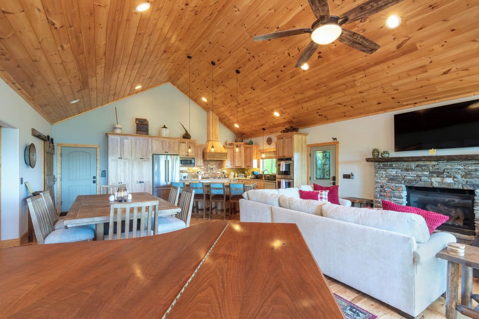 Open Floor Plan – Dining, Living and Kitchen View - Wide open main level connecting the dining area, kitchen island, living room, and stone fireplace under a cathedral ceiling.
