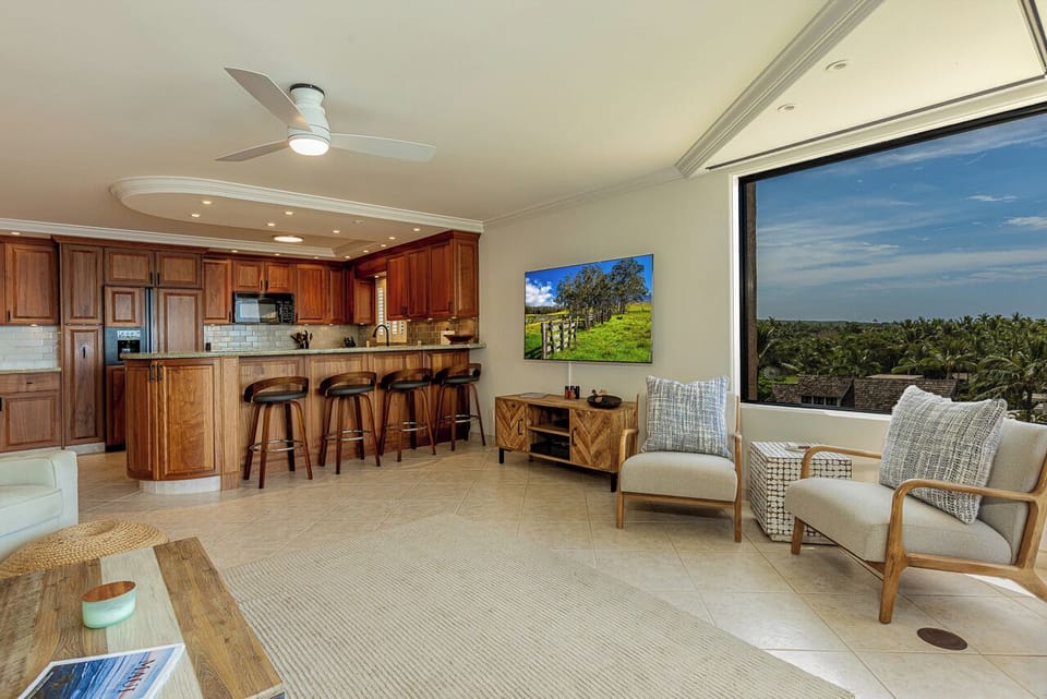 Relax in this open-concept living space featuring stunning tropical views, modern kitchen with breakfast bar, and comfortable seating perfect for your Hawaiian getaway.