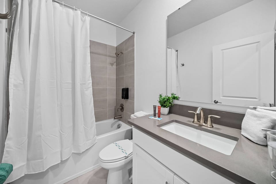 Experience a bright and inviting bathroom with sleek gray countertops and a spacious mirror that enhances the airy feel. Soft white towels and a touch of greenery create a charming atmosphere, perfect for your relaxation.