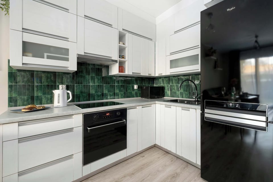 A clean, modern kitchen with white upper cabinets and lower dark cabinets features a built-in oven and black hobs. Above the stove and sink area, the wall is painted a deep, rich teal, adding a touch of color to the kitchen.