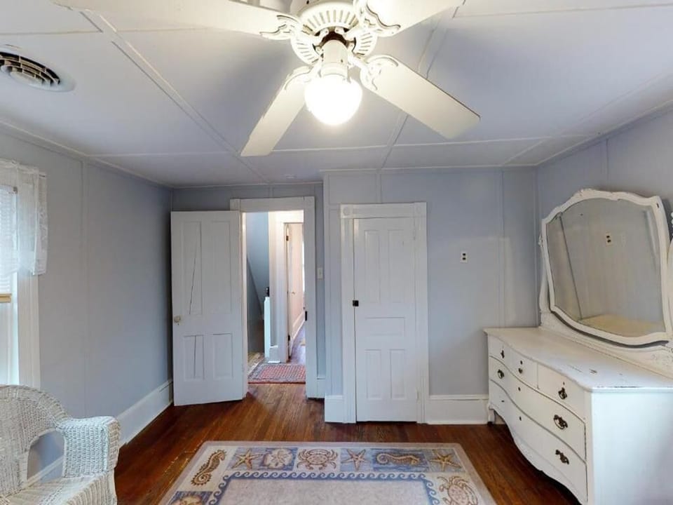 A cozy bedroom showcases a vintage dresser, white wicker seating, and a charming ceiling fan, enhancing its inviting ambiance.