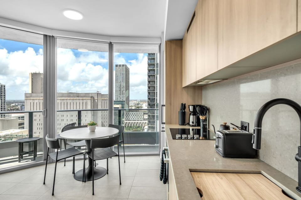Modern culinary convenience meets high-rise living! This sleek kitchen features light wood cabinetry, integrated appliances, and a built-in stovetop—all just steps from a bright dining area framed by stunning cityscape views.