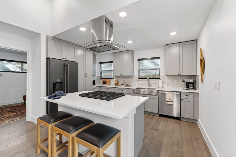 Modern kitchen with grey cabinetry, white quartz countertops, and a central island with a built-in cooktop.
