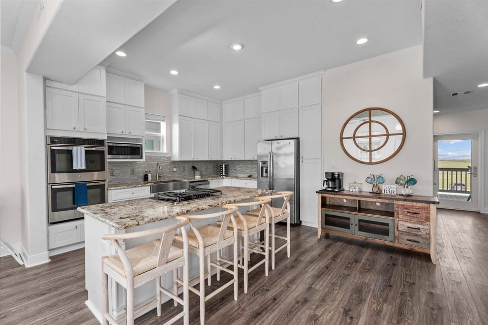 Bright open-concept kitchen with large island seating, modern appliances, white cabinetry, and granite countertops in this luxury Galveston beach house.