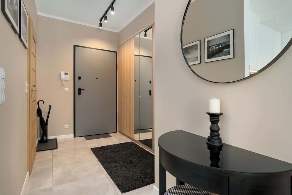 A small hallway or entrance area with a round mirror and a stylish sink or vanity. Neutral colors and simple décor give the space a modern look. The area is designed to be both practical and visually appealing.