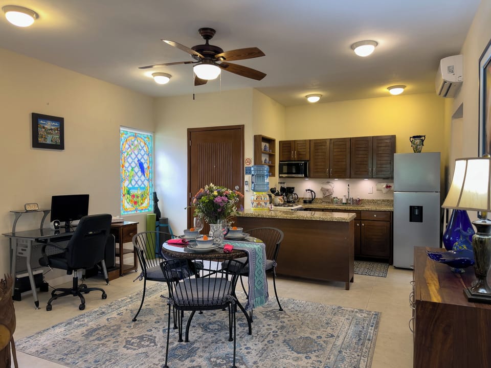 Abbey del Sol Apt 6 – Living/Dining Area with Workspace - Spacious open-plan living and dining area with ceiling fans, dining table, full kitchen, and a dedicated desk/workspace for remote work.