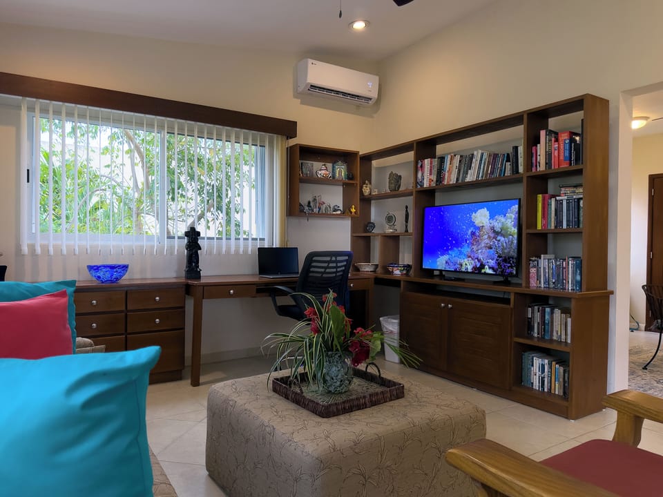 Abbey del Sol Apt 6 – Living Room TV, Bookshelf & A/C - Comfortable living room with A/C, a flat-screen TV, built-in bookshelves, and a desk area—easy for movie nights and longer stays.